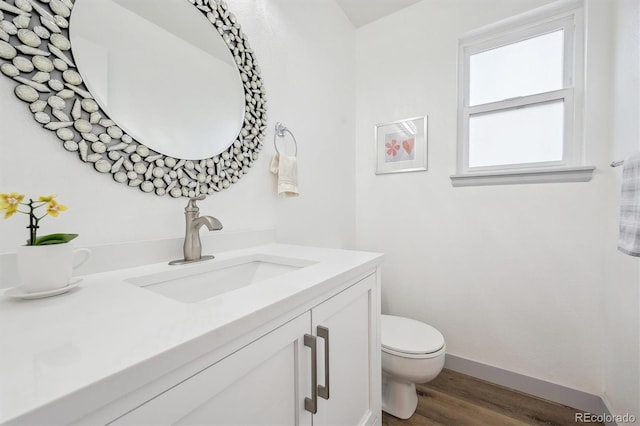 half bath featuring wood finished floors, toilet, vanity, and baseboards