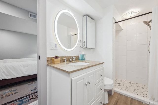 ensuite bathroom with a tile shower, wood finished floors, toilet, and vanity