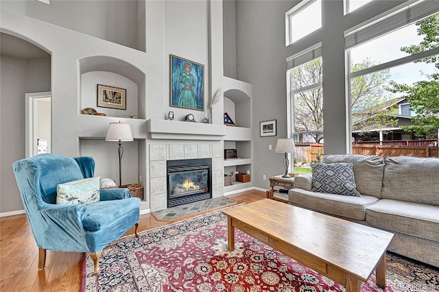 10653 W Parkhill Dr, Littleton, CO 80127 - living room featuring built in shelves, wood finished floors, a fireplace, a towering ceiling, and baseboards