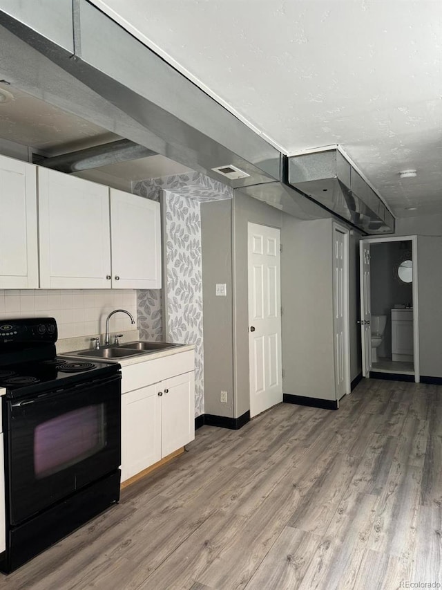 kitchen featuring light wood-type flooring, backsplash, black range with electric cooktop, sink, and white cabinetry