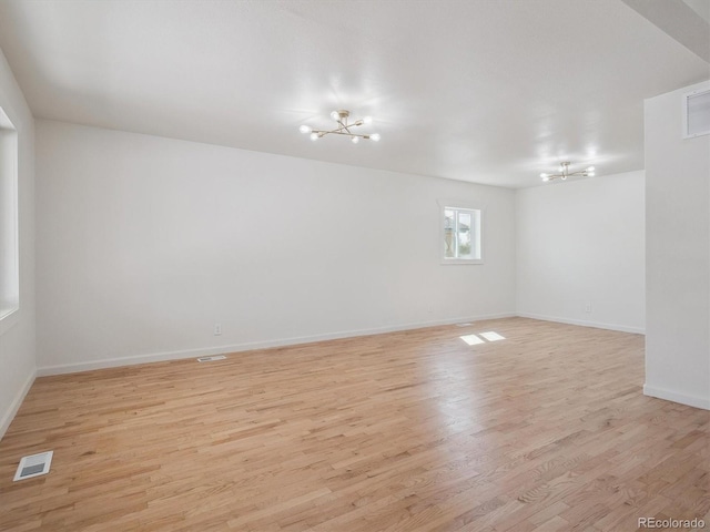 unfurnished room with visible vents, light wood-type flooring, and a notable chandelier