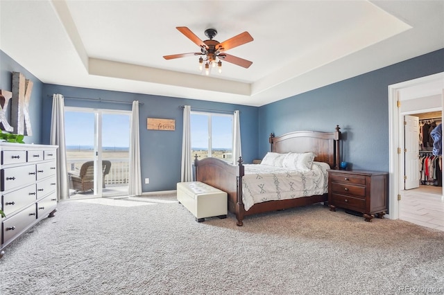 carpeted bedroom with access to outside, a tray ceiling, a spacious closet, and a ceiling fan