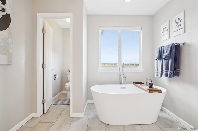 bathroom with a freestanding bath, baseboards, tile patterned flooring, and toilet