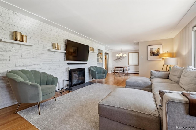 living room featuring wood finished floors, a chandelier, a baseboard radiator, and a stone fireplace