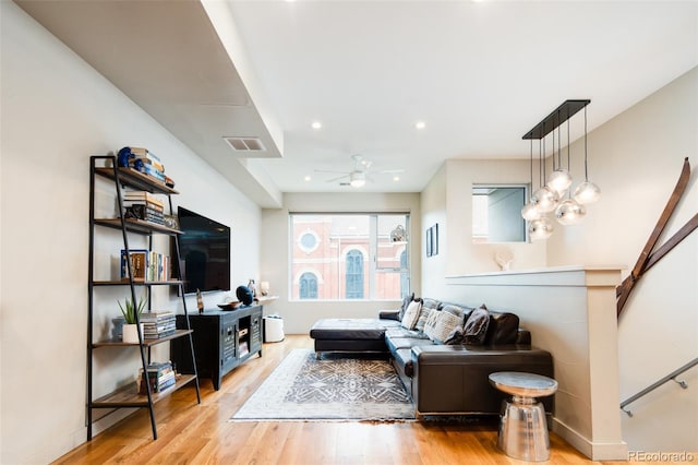 living room with ceiling fan with notable chandelier and light wood-type flooring