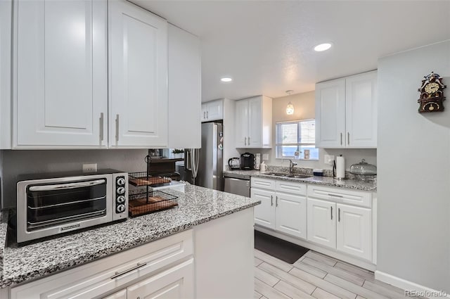 kitchen with stainless steel appliances, sink, light stone countertops, white cabinetry, and light hardwood / wood-style floors