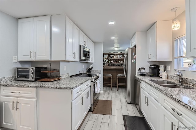 kitchen featuring sink, hanging light fixtures, stainless steel appliances, white cabinets, and light stone counters