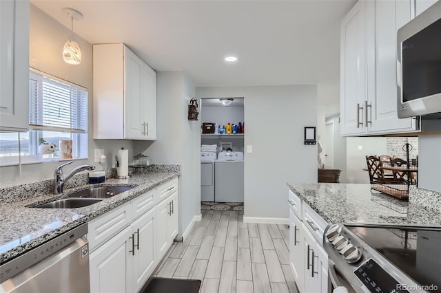 kitchen with white cabinets, hanging light fixtures, stainless steel appliances, washing machine and dryer, and sink