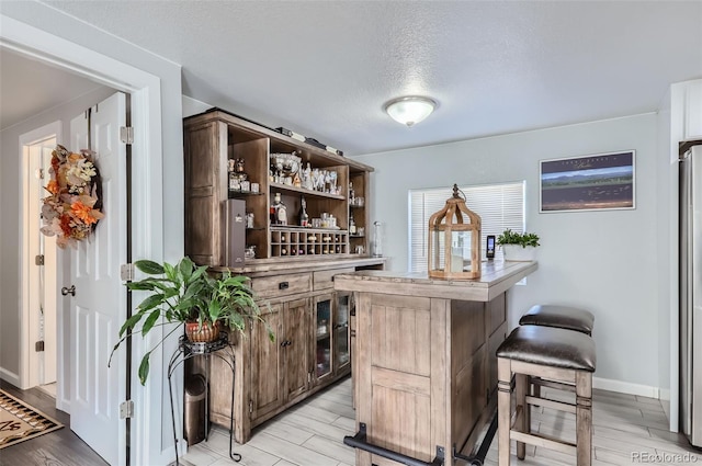 bar featuring a textured ceiling, light hardwood / wood-style flooring, dark brown cabinets, and stainless steel refrigerator