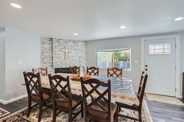 dining area featuring a textured ceiling, dark hardwood / wood-style flooring, and a brick fireplace