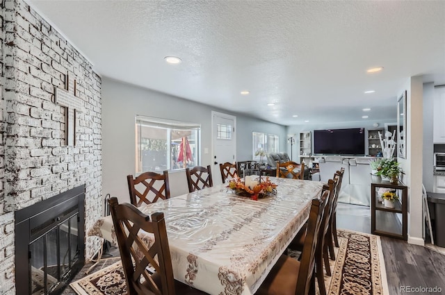 dining area featuring dark wood-type flooring, a textured ceiling, and a brick fireplace