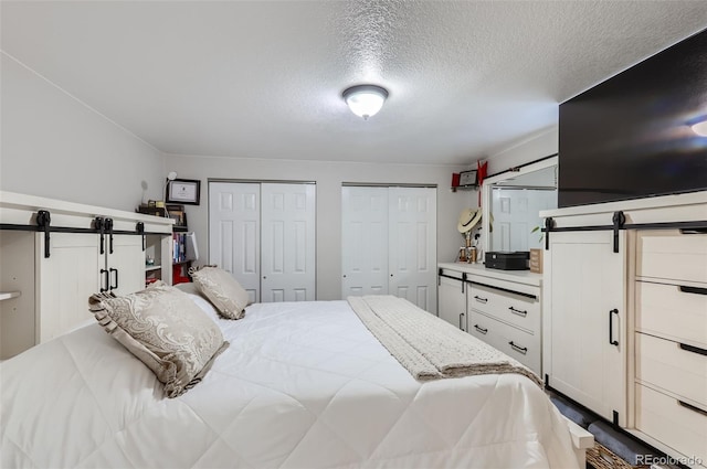 bedroom with a barn door, two closets, and a textured ceiling