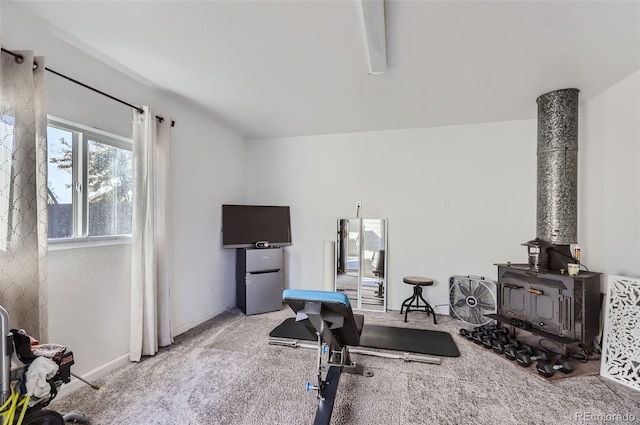 exercise room featuring a wood stove and light colored carpet