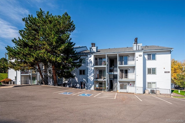 view of building exterior with fence, central AC, and uncovered parking