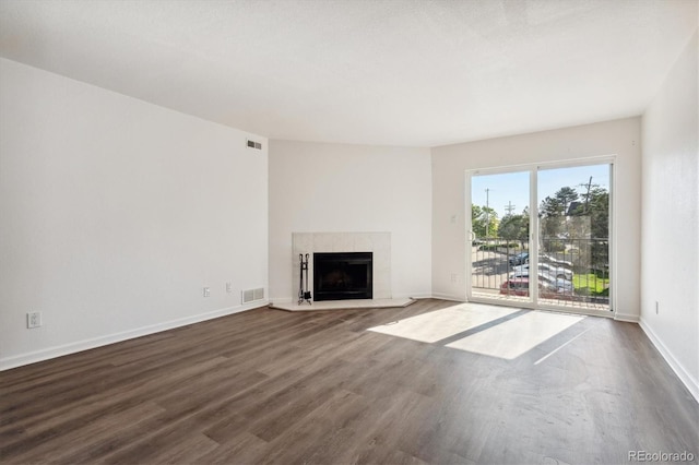 unfurnished living room with dark wood-type flooring, a fireplace with raised hearth, visible vents, and baseboards