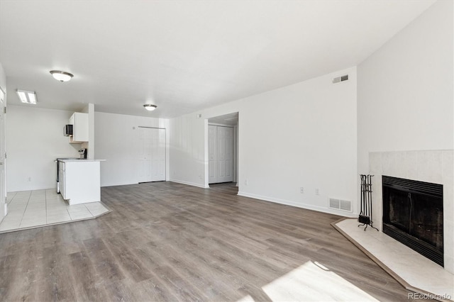 unfurnished living room featuring a tiled fireplace, visible vents, and light wood-style flooring