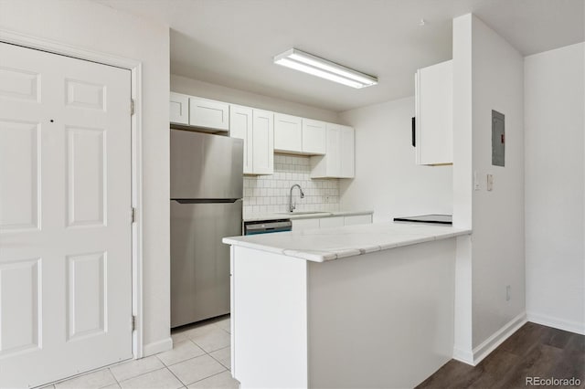 kitchen with a sink, backsplash, freestanding refrigerator, a peninsula, and white cabinets