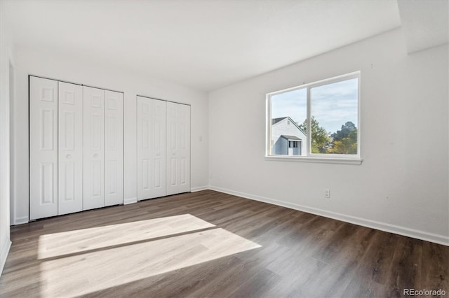 unfurnished bedroom featuring wood finished floors, baseboards, and two closets