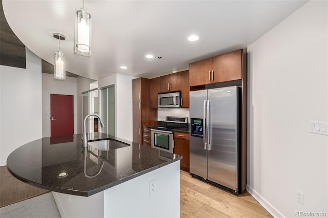 kitchen with sink, stainless steel appliances, dark stone counters, decorative light fixtures, and light wood-type flooring