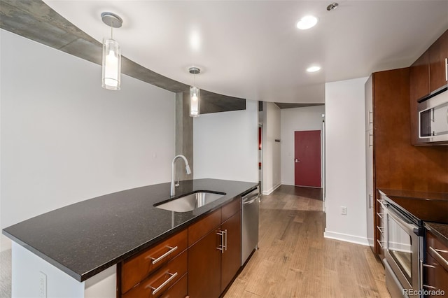 kitchen with dark stone counters, sink, hanging light fixtures, light wood-type flooring, and stainless steel appliances