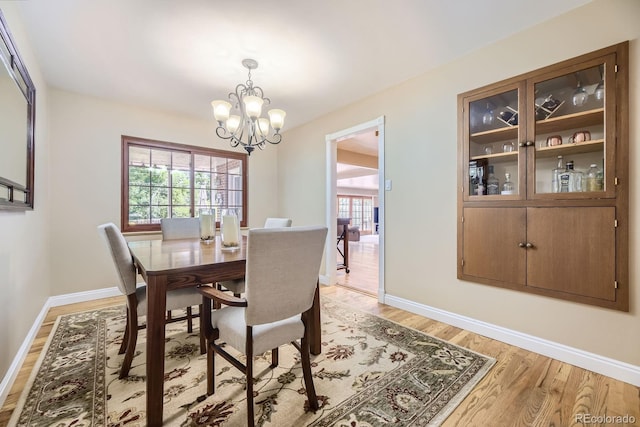 dining room featuring light wood-type flooring, a chandelier, baseboards, and a healthy amount of sunlight