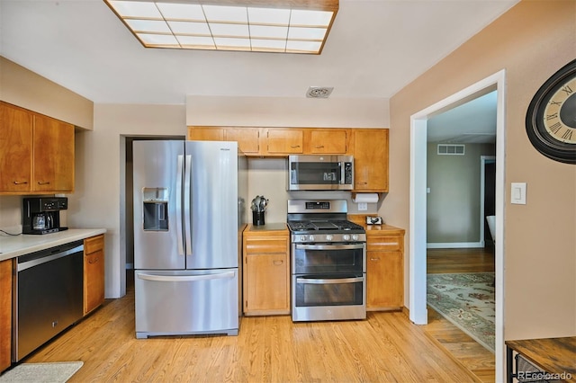 kitchen featuring light wood finished floors, stainless steel appliances, light countertops, and visible vents