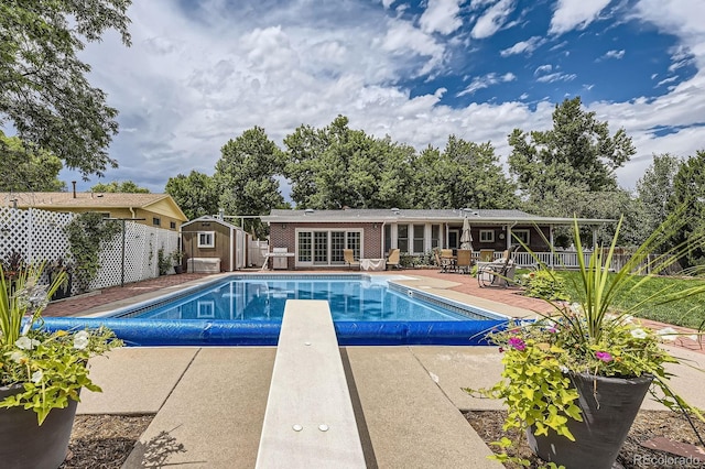 view of pool with a storage unit, a patio, a diving board, and a fenced backyard