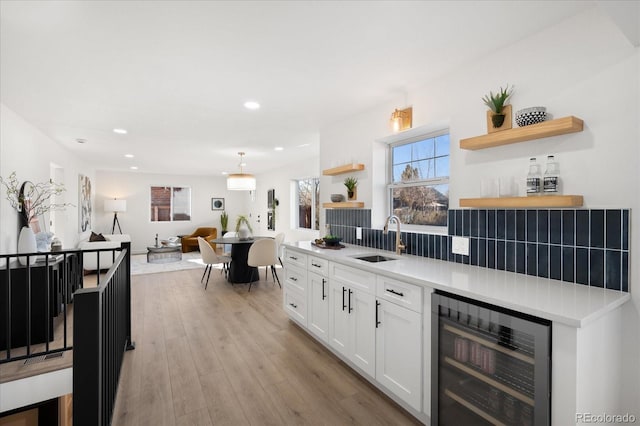 kitchen with pendant lighting, white cabinets, sink, wine cooler, and light hardwood / wood-style floors