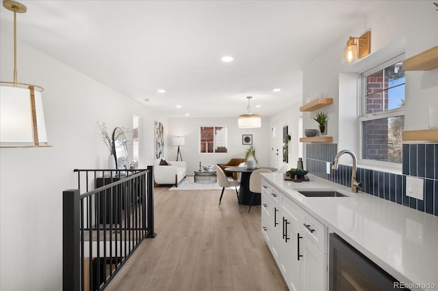 kitchen with white cabinetry, sink, beverage cooler, pendant lighting, and light wood-type flooring