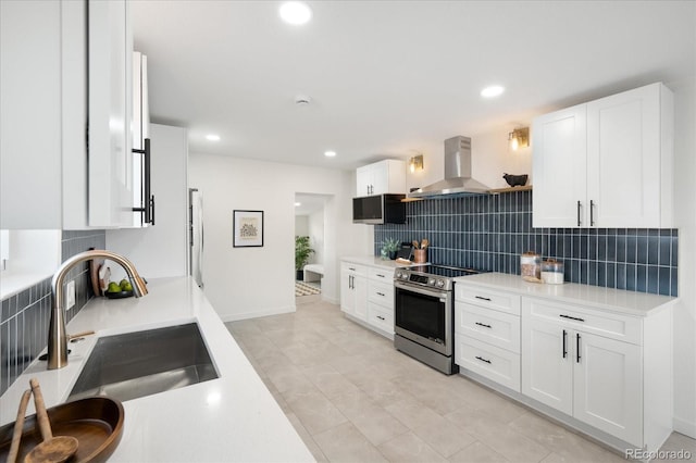 kitchen featuring electric range, sink, white cabinets, and wall chimney range hood