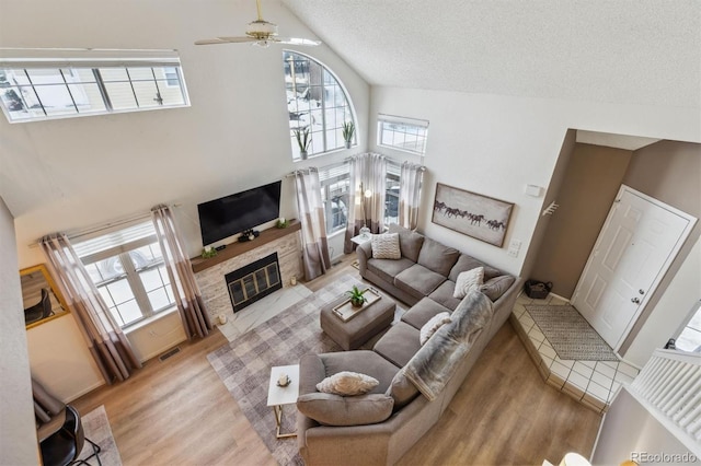 living room featuring a fireplace, visible vents, light wood-style floors, a textured ceiling, and high vaulted ceiling