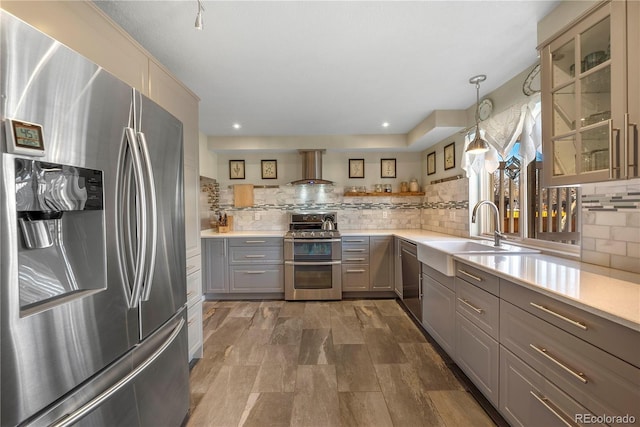 kitchen with sink, gray cabinetry, pendant lighting, stainless steel appliances, and wall chimney range hood