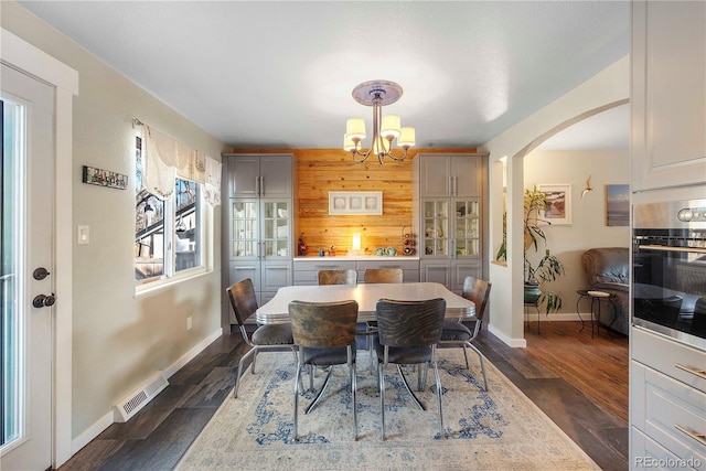 dining room with a notable chandelier, dark hardwood / wood-style flooring, and wood walls