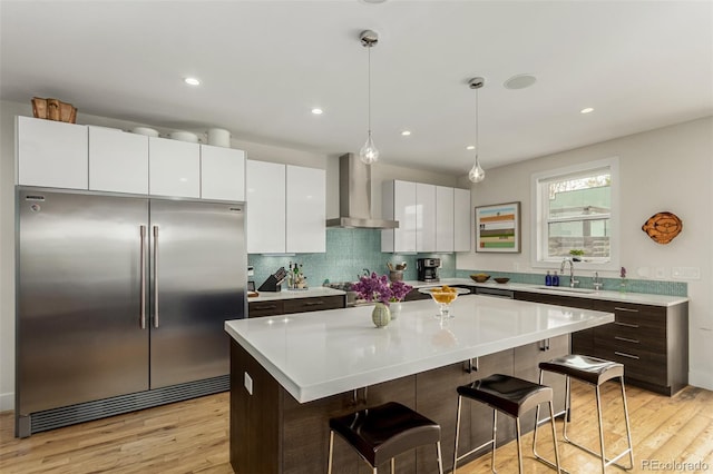 3168 W 29th Ave, Denver, CO 80211 - kitchen featuring stainless steel built in refrigerator, wall chimney exhaust hood, a breakfast bar area, light wood-style floors, and recessed lighting