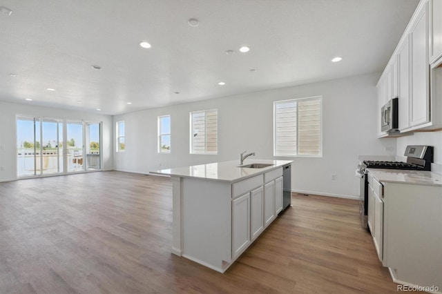 kitchen with white cabinets, a kitchen island with sink, light wood-type flooring, sink, and stainless steel appliances