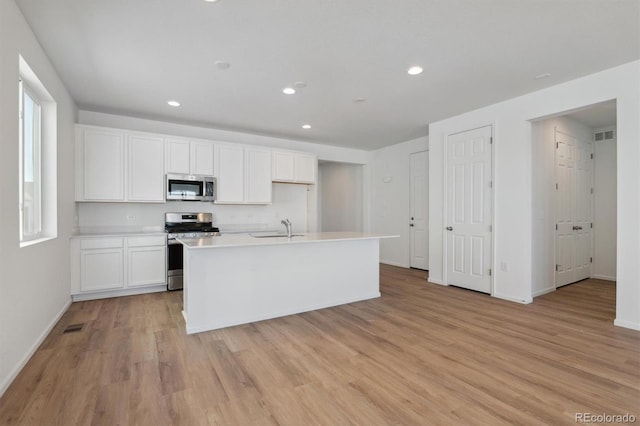 kitchen featuring an island with sink, stainless steel appliances, sink, light wood-type flooring, and white cabinetry