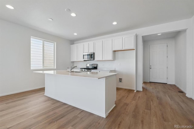 kitchen with appliances with stainless steel finishes, sink, white cabinets, light hardwood / wood-style flooring, and a kitchen island with sink