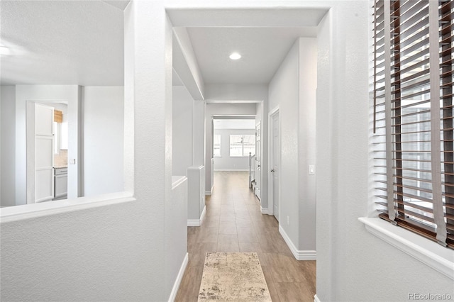 hallway with a textured wall, wood finished floors, and baseboards