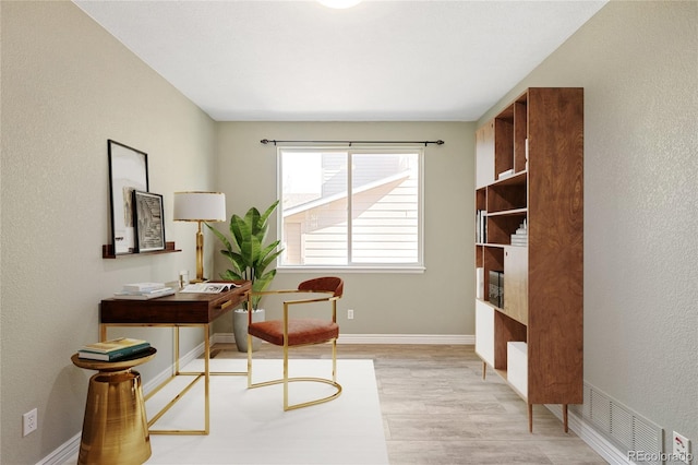 office space with light wood-style floors, visible vents, and baseboards