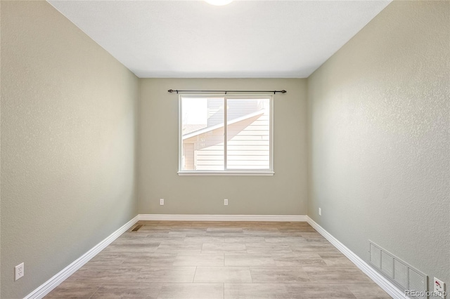 empty room with light wood-type flooring, baseboards, visible vents, and a textured wall