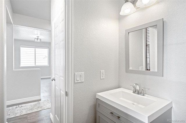 bathroom featuring a textured wall, baseboards, wood finished floors, and vanity