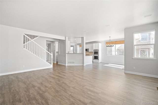 unfurnished living room featuring stairway, visible vents, light wood finished floors, and a chandelier