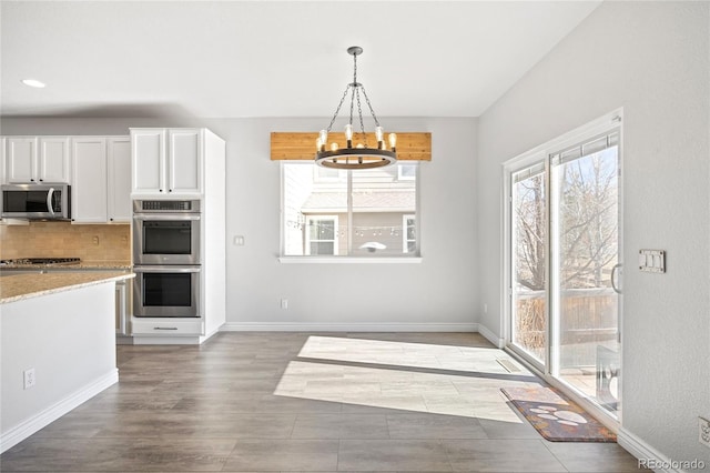 kitchen featuring baseboards, white cabinets, decorative backsplash, appliances with stainless steel finishes, and pendant lighting