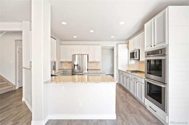 kitchen with stainless steel appliances, light wood-style floors, a peninsula, and light stone counters