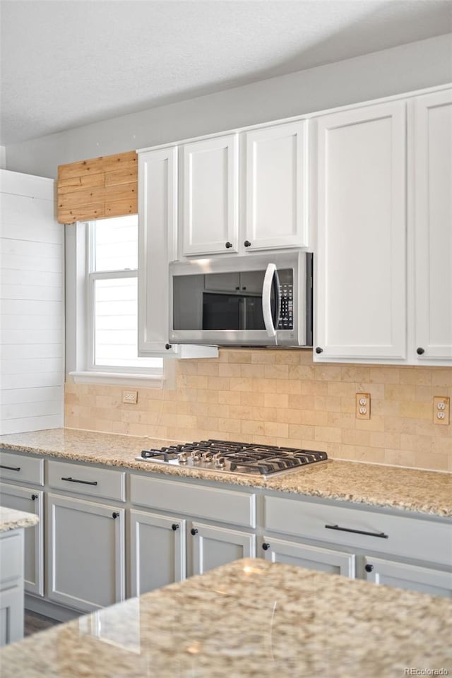 kitchen featuring white cabinets, appliances with stainless steel finishes, light stone countertops, and decorative backsplash