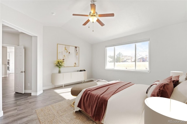 bedroom with ceiling fan, light wood-style flooring, baseboards, and vaulted ceiling