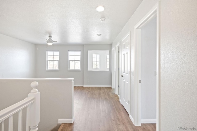 hall featuring a textured ceiling, light wood-style flooring, an upstairs landing, and baseboards