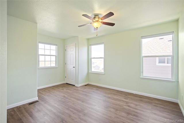 spare room with ceiling fan, a textured ceiling, wood finished floors, visible vents, and baseboards