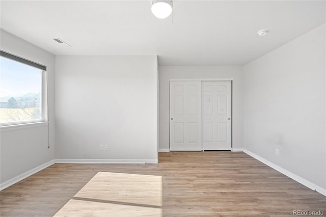 unfurnished bedroom featuring light wood finished floors, a closet, visible vents, and baseboards