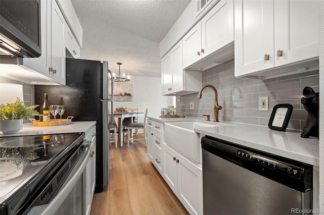 kitchen with light wood finished floors, dishwasher, light countertops, a textured ceiling, and white cabinetry